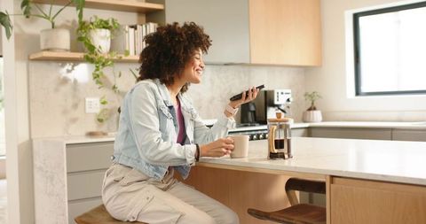African American woman enjoying morning coffee while talking on phone in bright kitchen