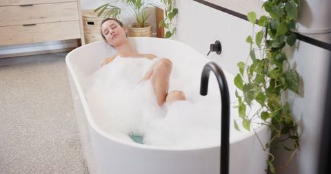 Woman Relaxing in Freestanding Bathtub Amid Bubbles and Plants