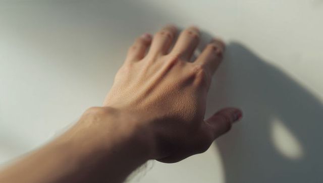 Resting hand casting soft shadow on pale wall with chipped nail polish closeup