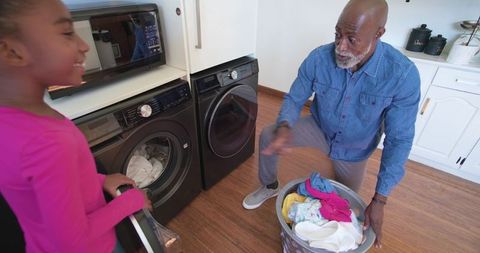 Multigenerational african american family loading front-load washer in modern laundry room
