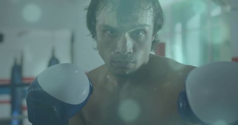 Intense boxer guarding with blue gloves closeup in boxing gym training