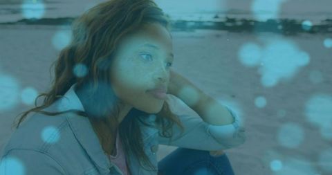 Contemplative young woman sitting on shore, gazing toward horizon with blue bokeh