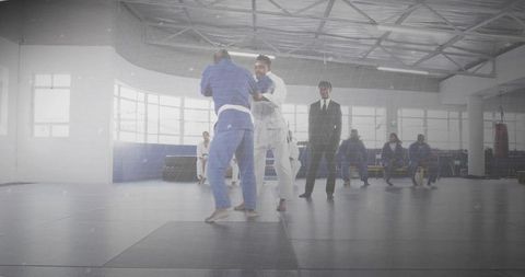 Sparring martial artists in blue and white gis during dojo training session with coach observing