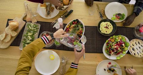 Diverse friends sharing rustic communal dinner around wooden table, pouring water and serving roast