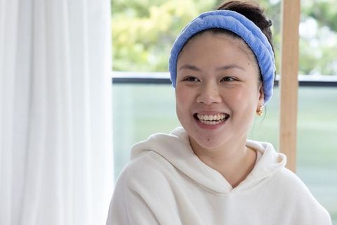 Smiling young woman wearing blue headband and white hoodie during morning skincare routine