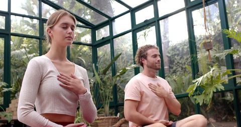 Couple meditating in serene glass-walled garden room