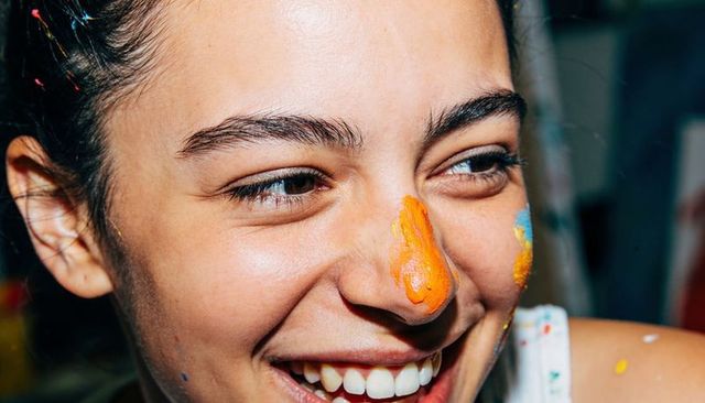 Teen girl smiling with paint on face during messy creative painting session closeup candid