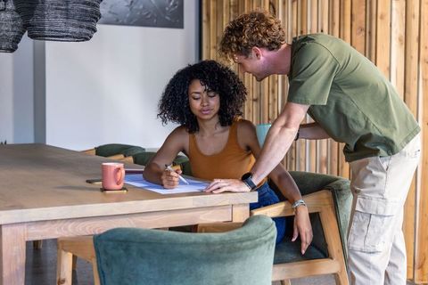 Diverse team collaborating at wooden table woman writing while man pointing to documents
