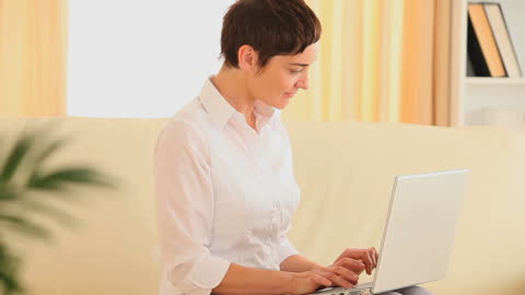 Happy Woman Using Laptop on Sofa in Bright Living Room