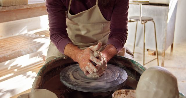 Close-up of an artist's hands molding clay on a pottery wheel, creating a ceramic bowl. Perfect for use in websites or publications about craftsmanship, creative arts, handmade items, or pottery making techniques. Great for illustrating the art of ceramics, highlighting the skill involved in crafting pottery.