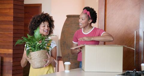 Women unpacking plant at home together in cheerful mood