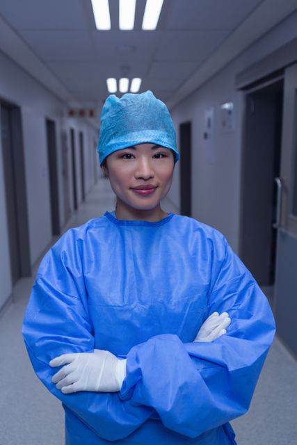Front view of female surgeon with arm crossed standing in corridor at hospital