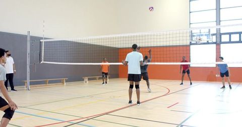 Indoor volleyball players competing, jumping and blocking at net in bright gymnasium