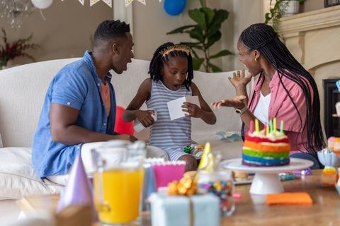 African american family celebrating birthday at home, child opening surprise card and birthday cake