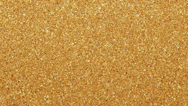 Gold glitter texture with sparkling metallic flakes and shimmering bokeh highlights macro