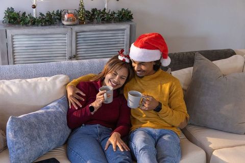 Couple cuddling on sofa with santa hat and mugs, cozy christmas morning at home