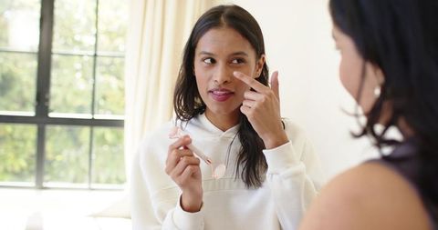 Diverse women using rose quartz facial roller and sharing skincare moment by sunny window