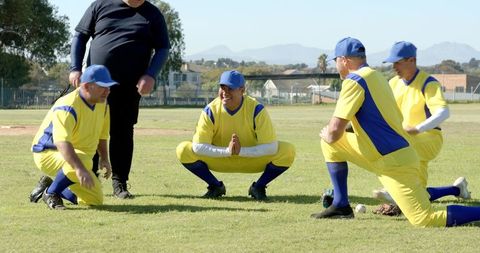 Community baseball team stretching and warming up on sunny grass field in yellow uniforms