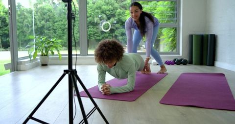 Fitness coach assisting client holding plank pose on purple mat in bright home gym