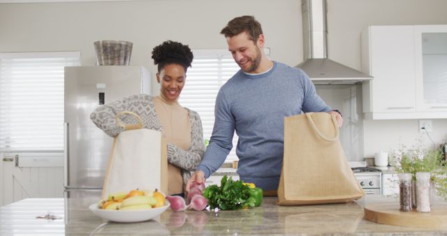 Image of happy diverse couple unpacking groceries in kitchen. Love, relationship and spending quality time together at home.