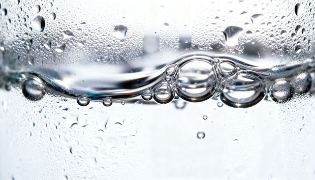 Macro water bubbles forming glossy cluster in clear glass with condensation and droplets