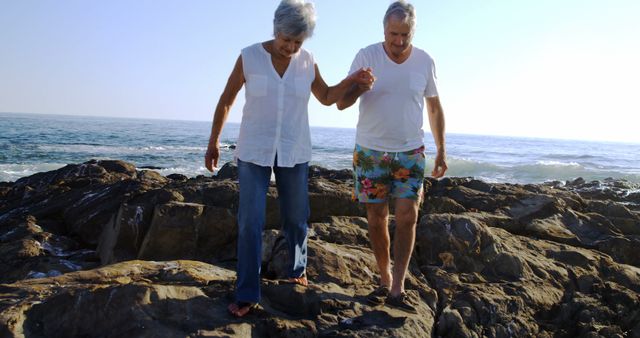 Happy senior caucasian couple holding hands and walking on rocks by sea. Retirement, relationship, love, togetherness, free time and relaxing, unaltered.