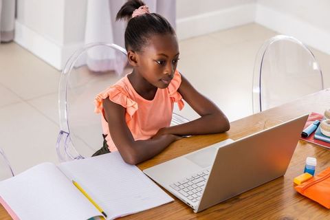 African girl studying on laptop at minimalist home desk for remote learning and homework