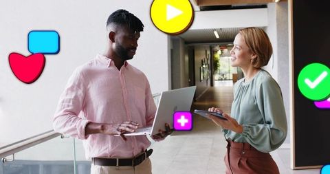 Coworkers collaborating with laptop and tablet in modern corridor with digital app icons