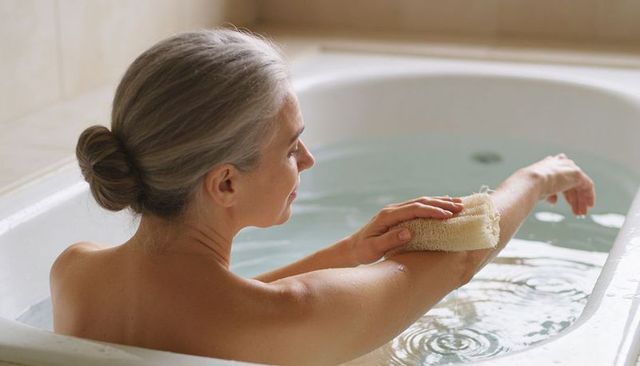 Mature woman soaking in bathtub while cleansing forearm with natural loofah for relaxation