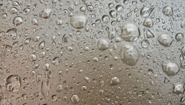 Close-up water droplets beading on glass creating reflective texture and abstract pattern
