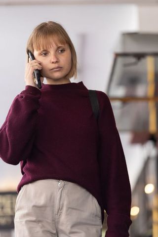Pensive commuter talking on smartphone wearing burgundy sweater carrying backpack at station