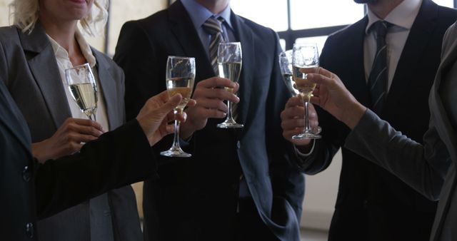 This photo shows business colleagues gathered to celebrate with champagne while at an office party. The individuals are dressed in formal attire, highlighting a professional environment. Suitable for use in topics related to business celebrations, corporate events, team bonding, and professional success.