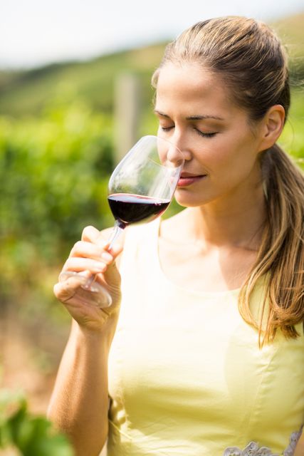 Female vintner smelling glass of wine in vineyard