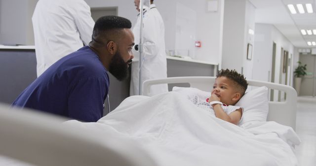 African american male doctor talking to child patient laying in bed at hospital. Medicine, healthcare, lifestyle and hospital concept.