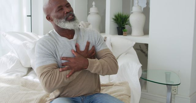 African American man clutching his chest in pain at home. He appears to be experiencing discomfort, a medical emergency.