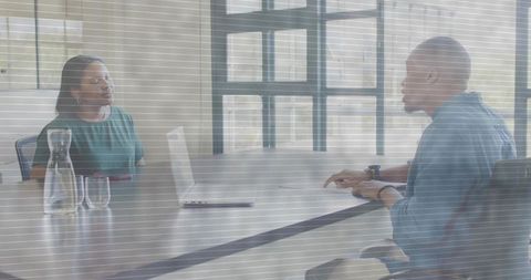 Two colleagues discussing strategy in bright boardroom with laptop and water carafe