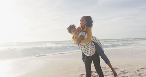 Playful Couple Enjoying Piggyback on Beach at Sunset