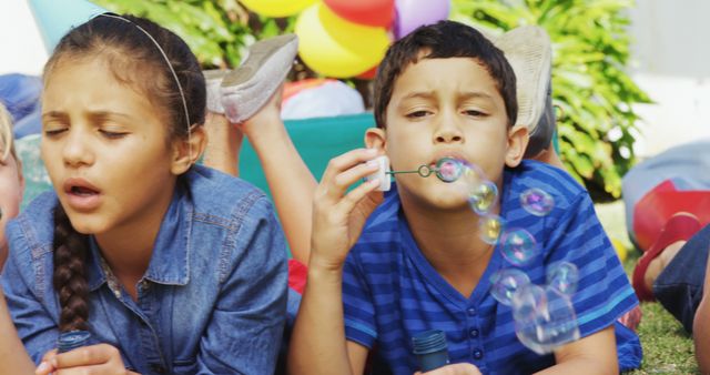 A young girl and boy are enjoying a playful moment blowing bubbles at an outdoor event, with copy space. Their expressions of concentration and delight capture the carefree joy of childhood.