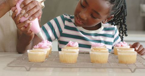 African american grandparent guiding grandchild decorating cupcakes, home baking bond
