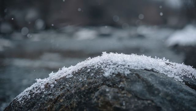 Snow-covered river rock closeup with frost crystals and flowing water bokeh