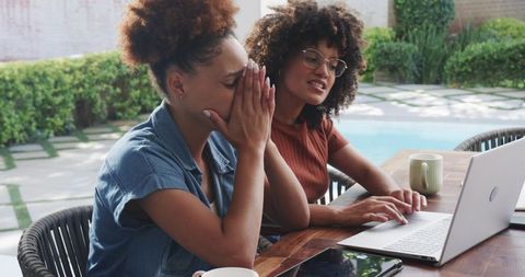 Two African American Women Collaborating Outdoors at Poolside Workspace Using Laptop
