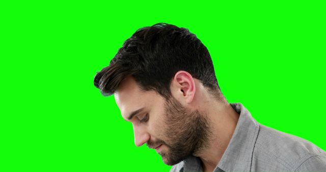 Man looking down with thoughtful expression against vibrant green background. Useful for designs requiring a pensive mood, introspective contexts, profile shots, or isolated backgrounds for easy editing.
