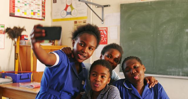 Group of African schoolgirls taking selfie together in classroom, wearing school uniforms. Suitable for use in educational themes, promoting friendship, technology in schools, and social interactions among students.