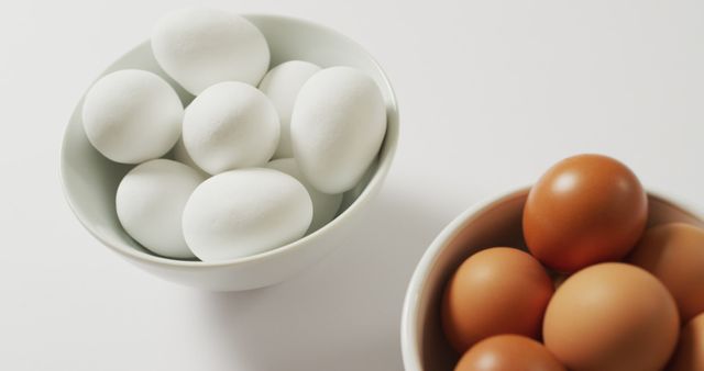 Close up of two bowls full of brown and white eggs with copy space on white surface. food and nutrition concept