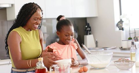 African american mother guiding daughter while baking together in bright modern kitchen