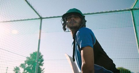 Young cricketer practicing in batting cage wearing green helmet and blue training jersey