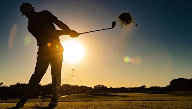 Sunset golfer swinging on fairway with flying divot and dramatic backlight lens flare