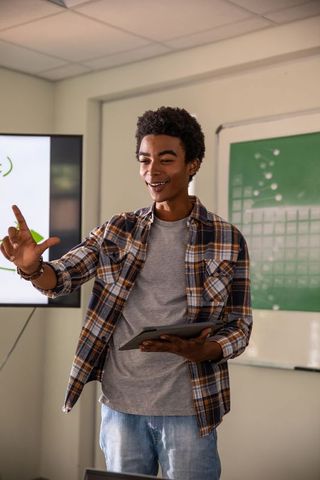 Young African American Student Presenting with Tablet in Modern Classroom, Engaging Peers