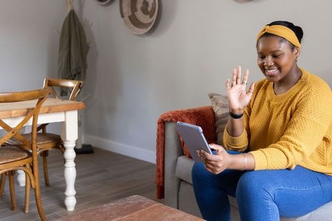 African american woman waving on tablet during video call in cozy modern living room