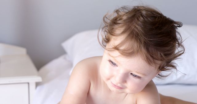 Cute baby seated on white bed in the bedroom - Download Free Stock Photos Pikwizard.com